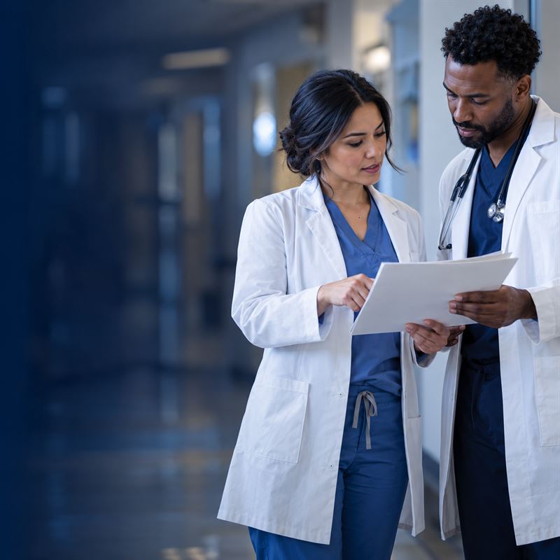 A nurse practitioner and a physician in white coats reviewing notes in a clinic hallway